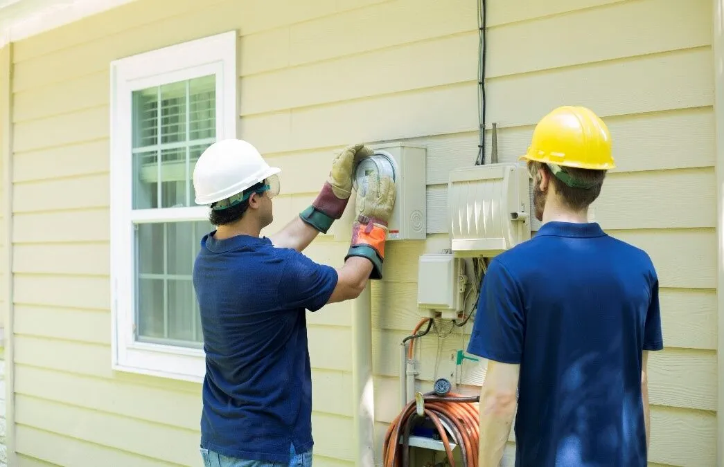 Two men working together on an electrical panel outside