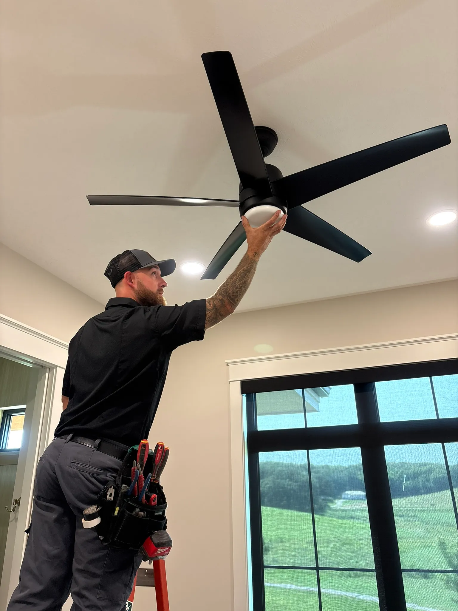 Electrician installing a ceiling fan with light kit in a Council Bluffs bedroom